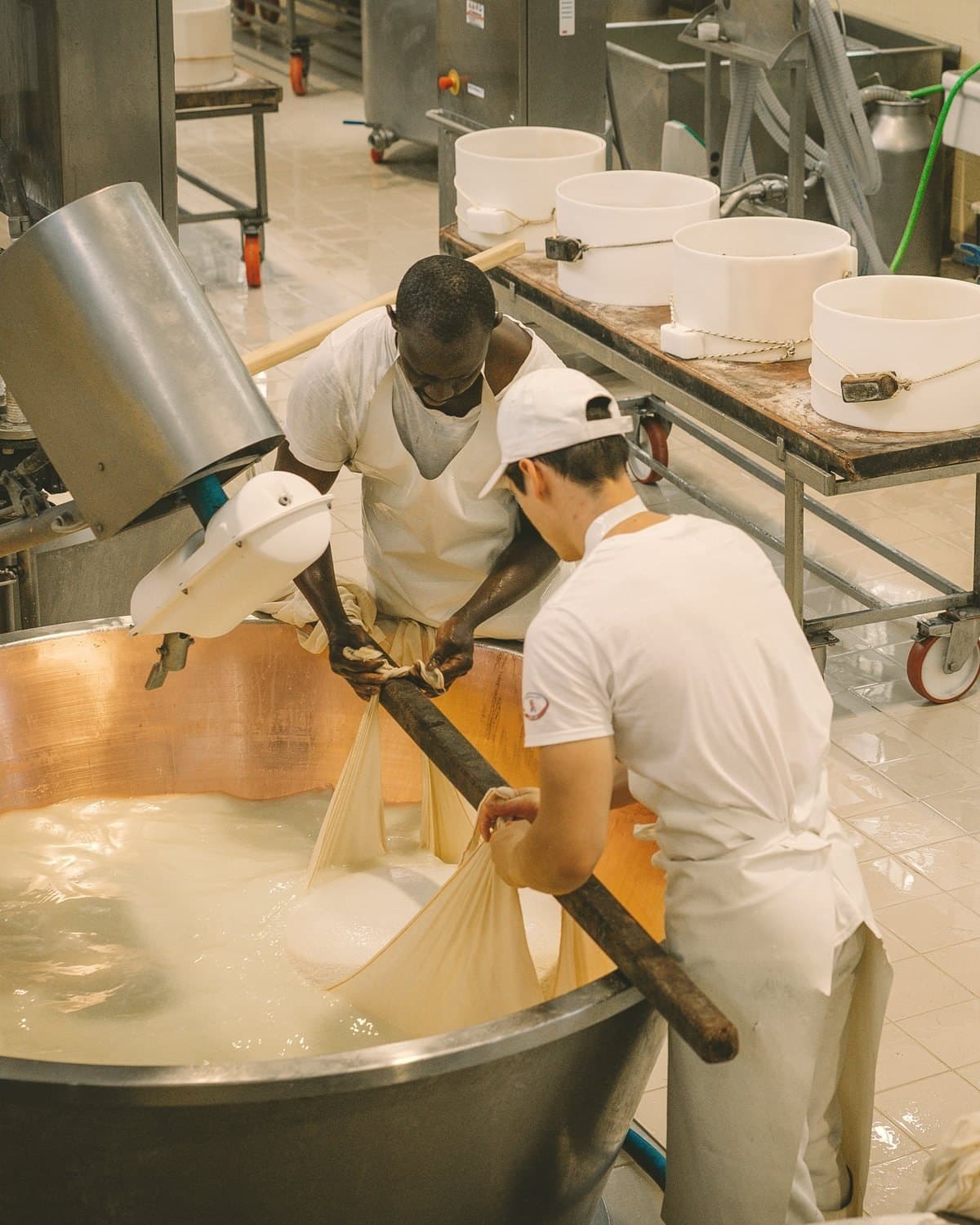 Two cheesemakers lifting curd from a copper vat